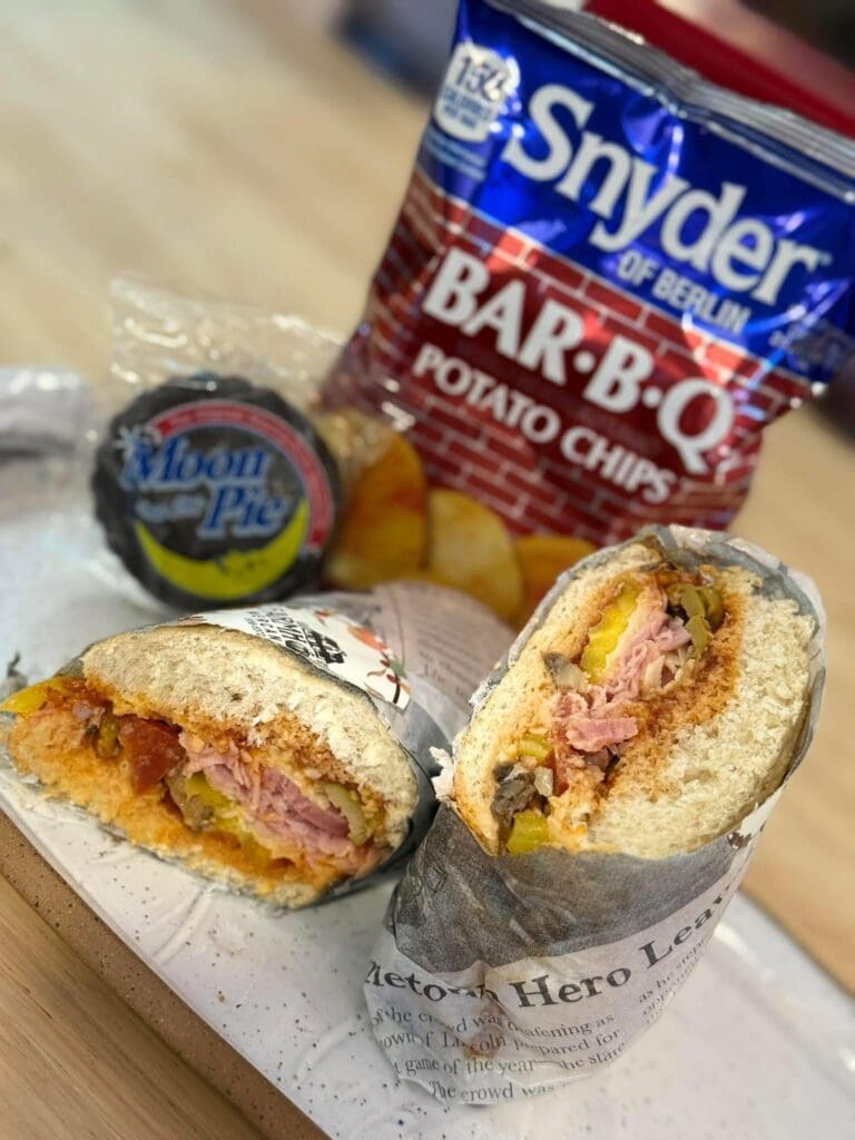 Two halves of a deli wrap filled with ham, cheese, and diced peppers on a plate, with a bag of chips in the blurred background.