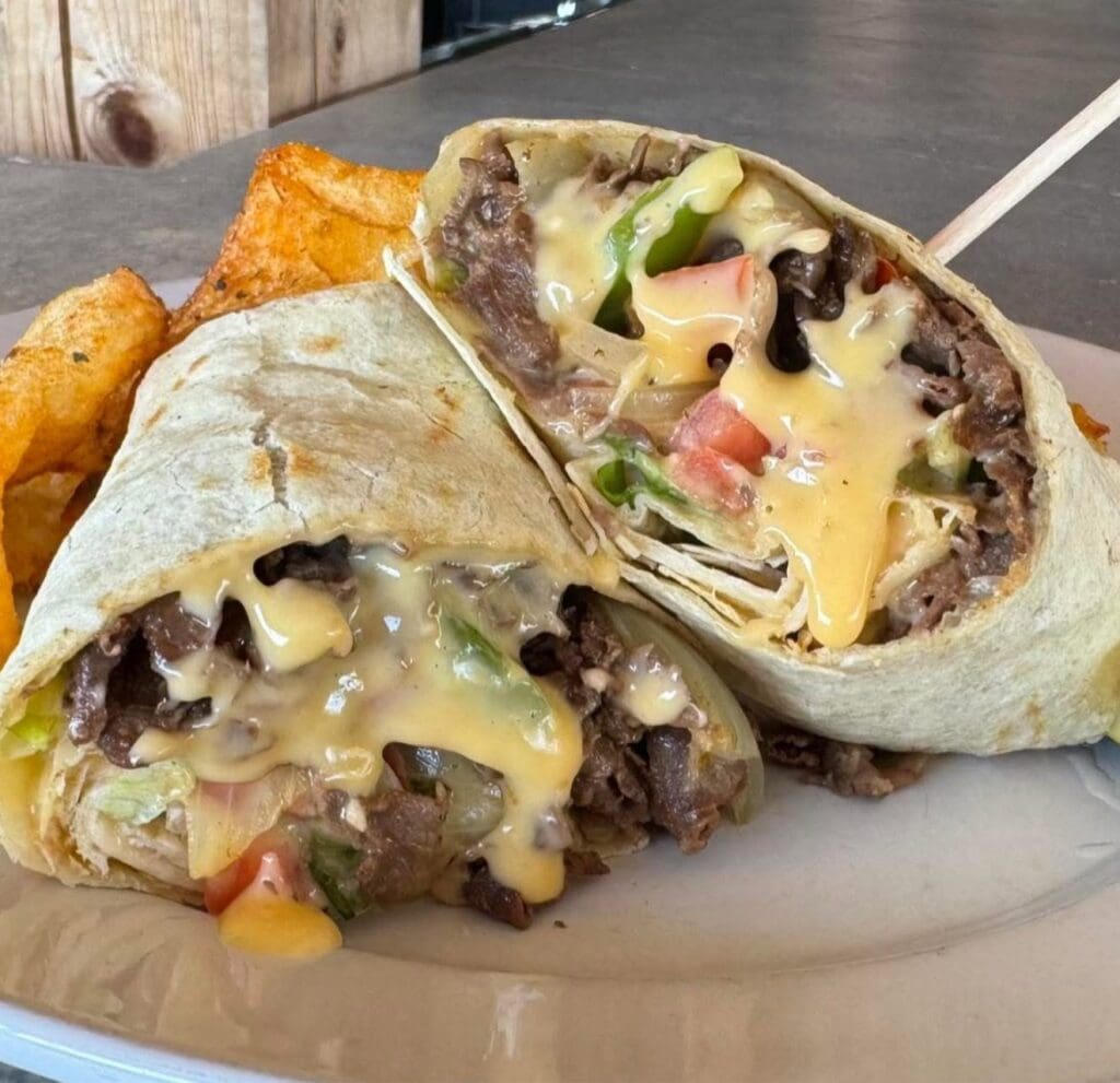 Two halves of a beef quesadilla filled with melted cheese, tomatoes, lettuce and peppers on a plate.