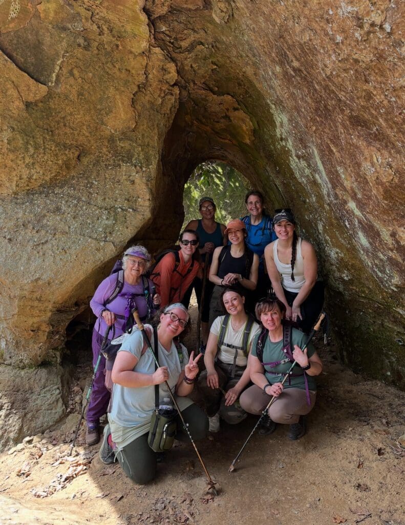 Group of hikers posing inside a rocky tunnel with trekking poles and backpacks.