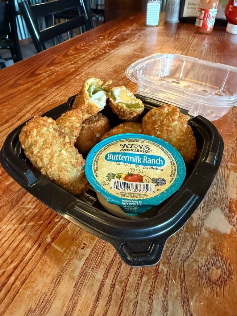 Fried bite-sized snacks in a black tray with a blue Ken's Buttermilk Ranch dip container on a wooden table.