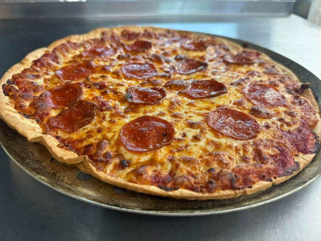Pepperoni pizza on a round crust resting on a metal baking tray in a kitchen setting.
