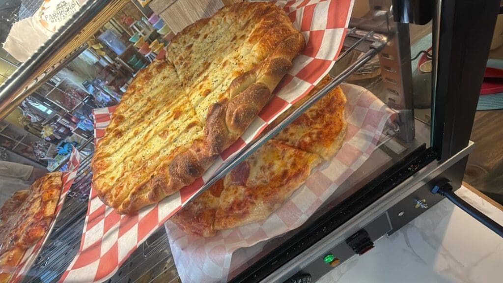 Two cheese pizzas on red-and-white checkered paper inside a glass display case at a pizzeria.