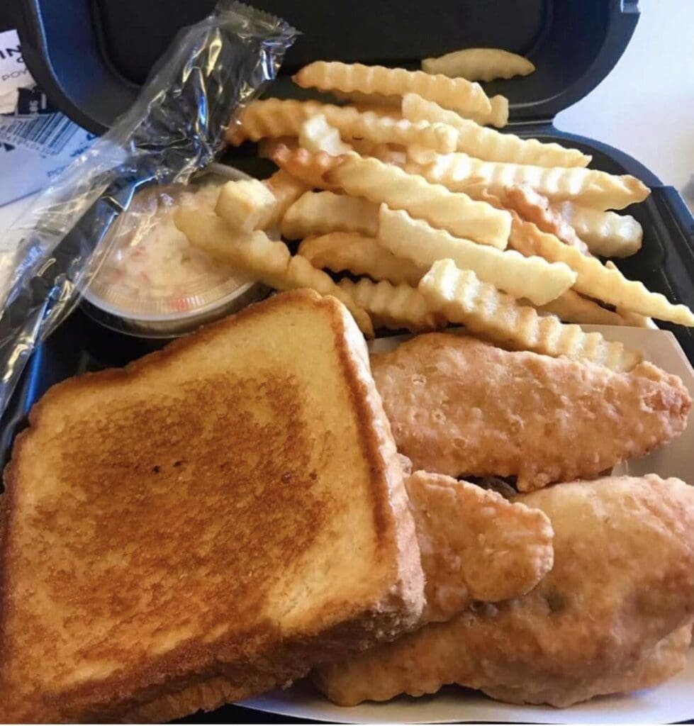 Takeout box with fried chicken tenders, toasted sandwich slices, and crinkle-cut fries; a dipping sauce container in the box.