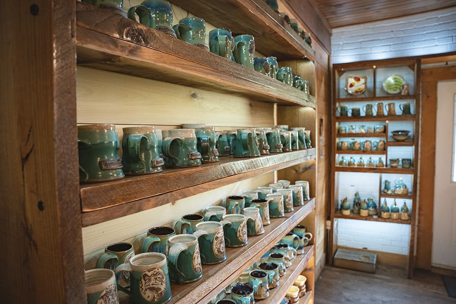Rows of turquoise ceramic mugs on wooden shelves in a pottery shop, with a bright display on the right wall