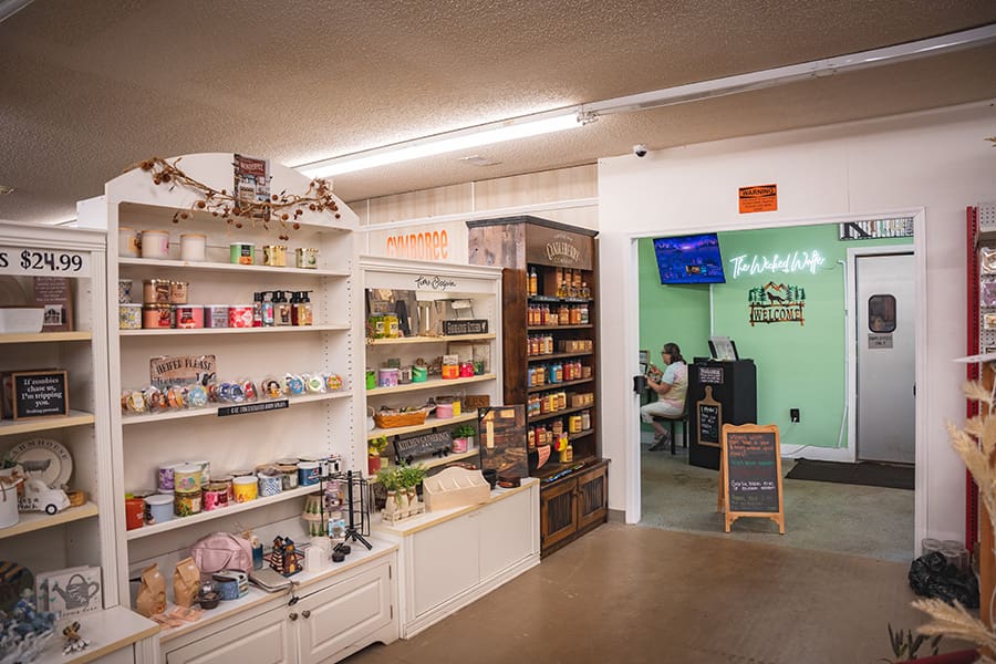 Gift shop aisle with white shelves full of mugs, candles, and decor, leading to a counter and a green-walled lobby referenced in the background.