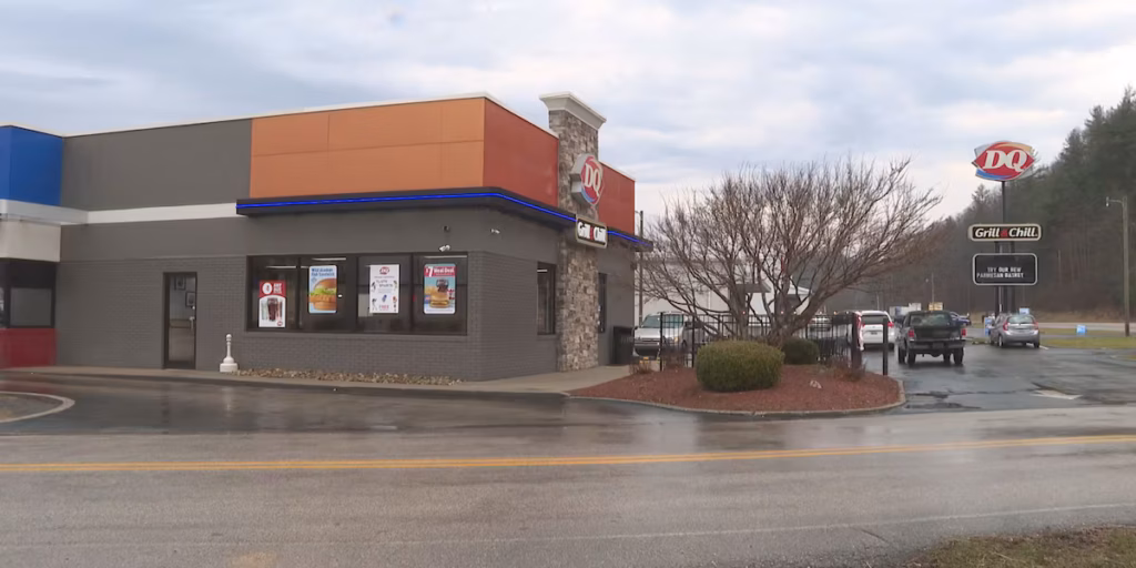 Dairy Queen restaurant with drive-thru, brick and stone facade, blue neon trim, and several cars in the wet parking lot.