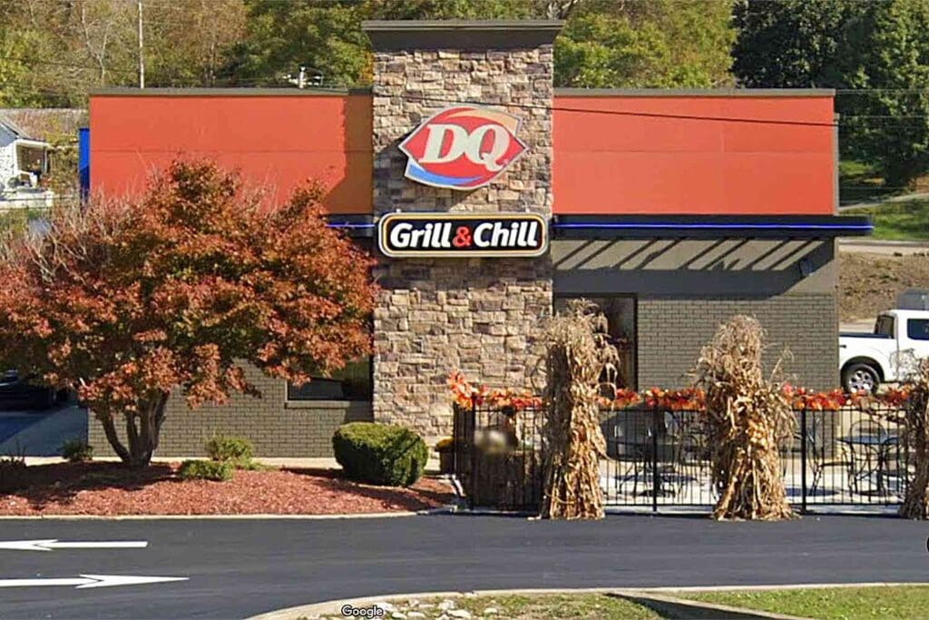 Front view of a Dairy Queen Grill & Chill restaurant with orange walls, a stone column, and autumn decor along a fence line.