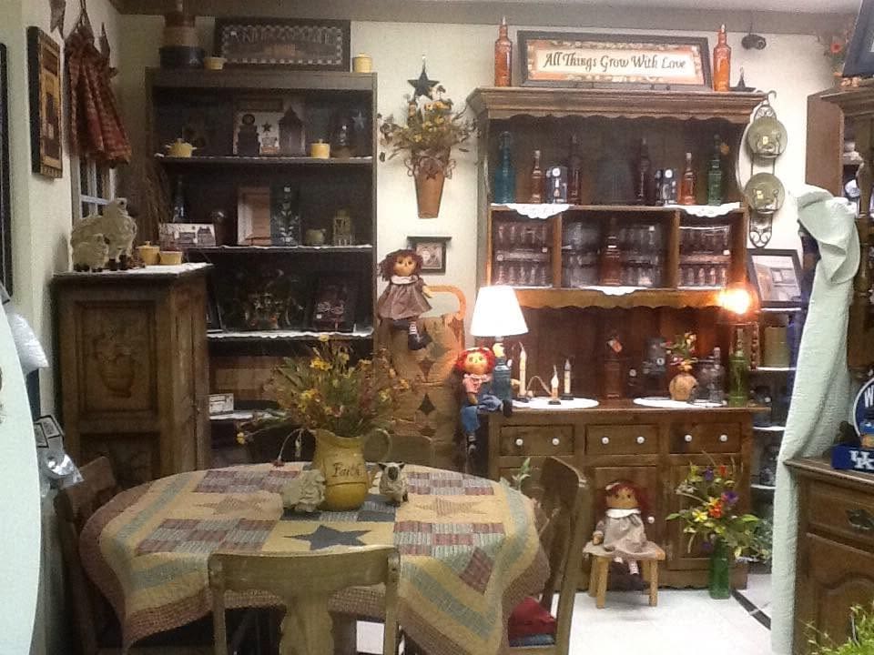Cozy antique shop interior with a patchwork table, vintage furnishings, and dolls on display shelves.