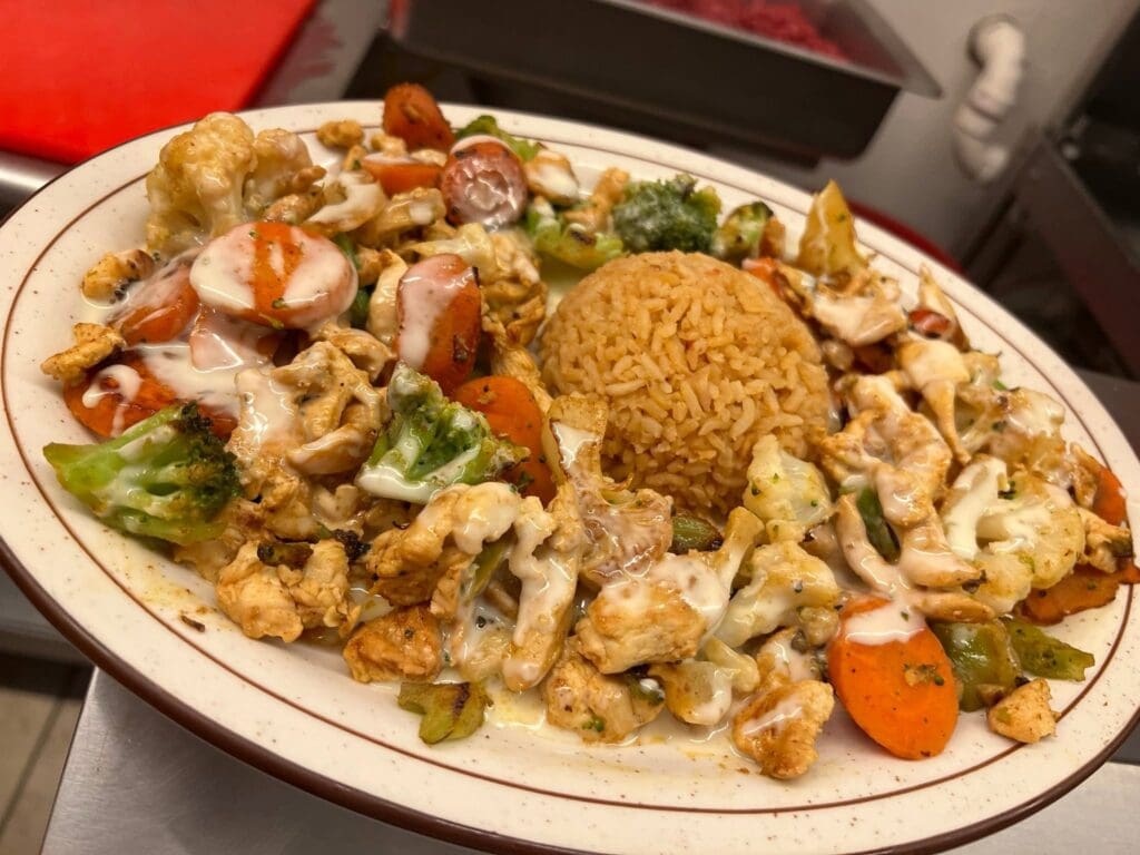 Plate with fried chicken pieces, broccoli, cauliflower, carrots, and brown rice with a creamy sauce drizzle.