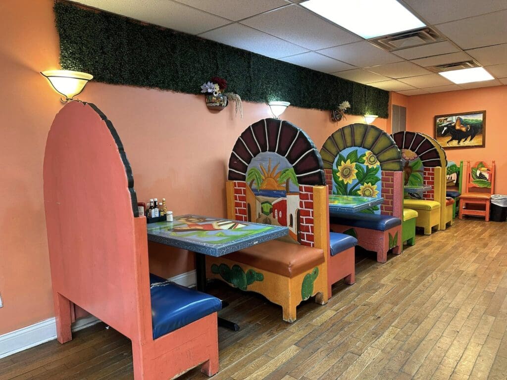 Colorful kids' restaurant with orange walls, blue cushioned booths, and painted arches along a long wall under a ceiling garlanded with green foliage.