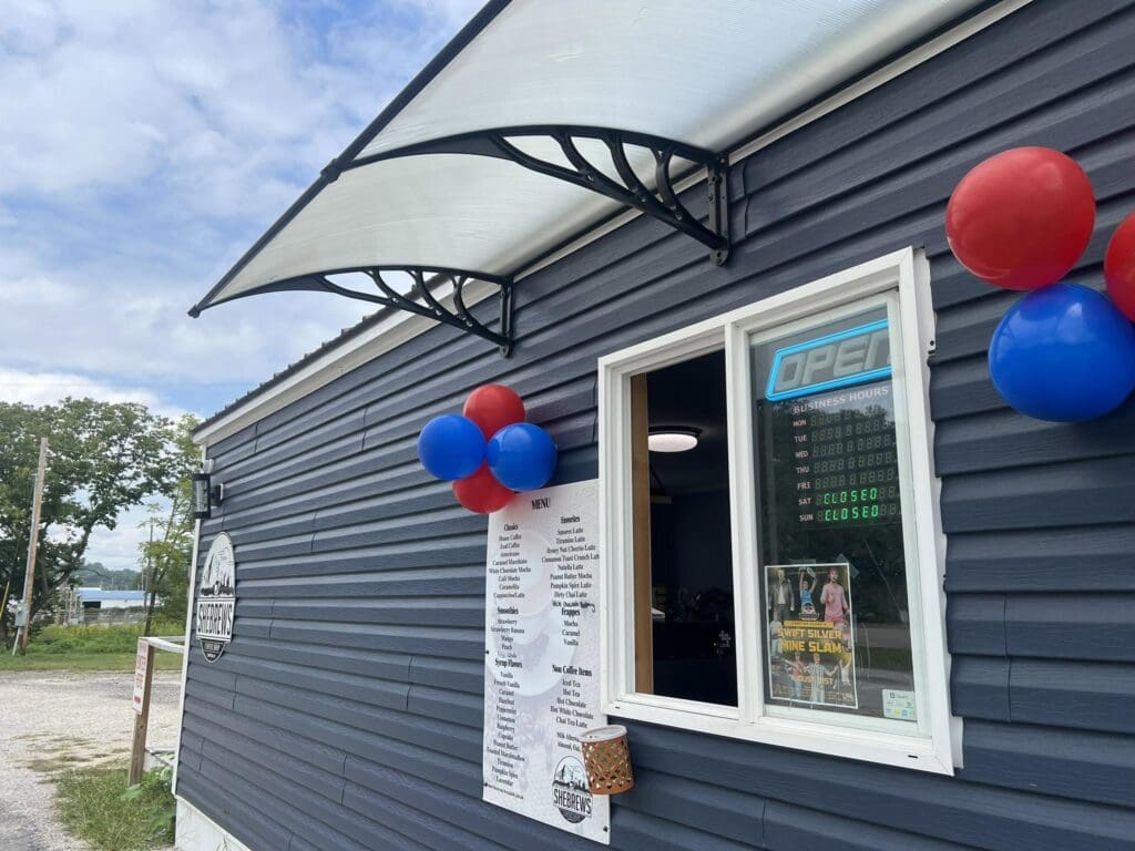Blue storefront with a translucent arched awning, open window, and red/blue balloons outside.